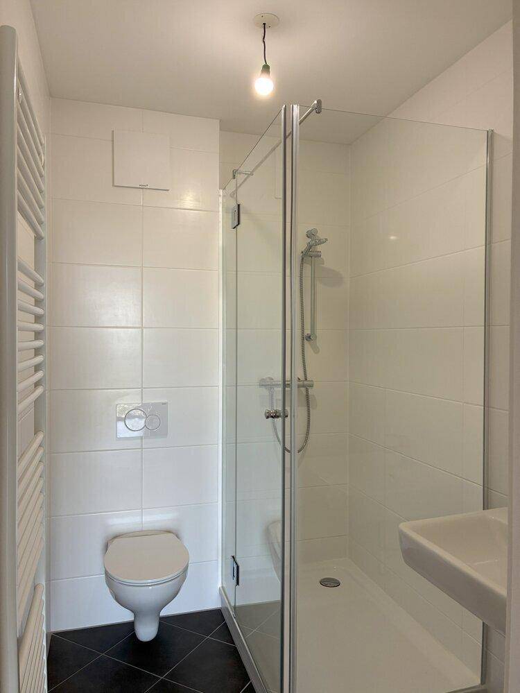 Modernes Badezimmer mit Dusche, WC, Handtuchheizkörper und dunklen Bodenfliesen.