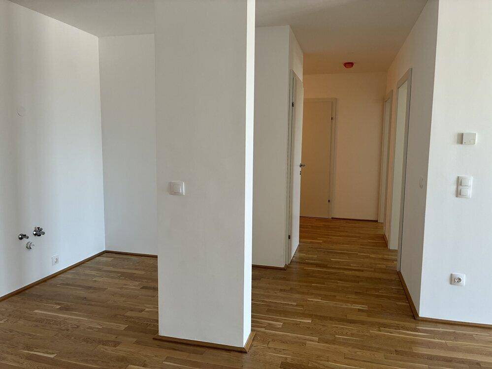 Heller Flur mit Holzboden und weißen Wänden, der zu weiteren Räumen führt.