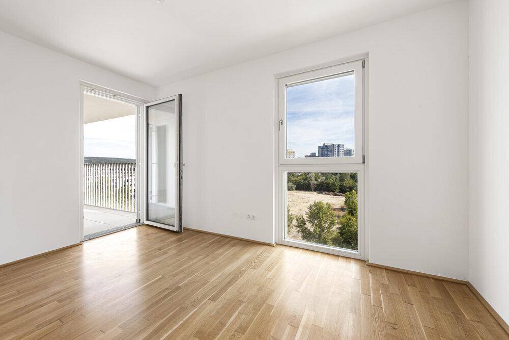 Helles Zimmer mit Parkettboden, großem Fenster und Zugang zu einem Balkon mit Weitblick.