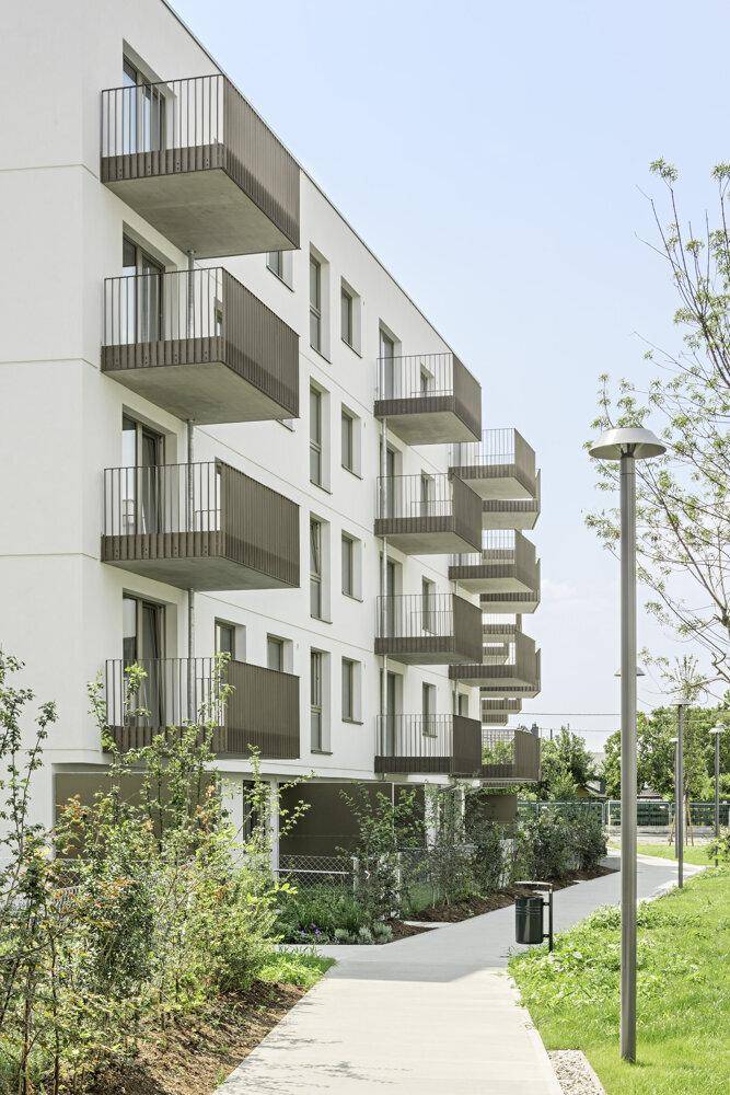 Moderne Wohngebäude-Fassade mit zahlreichen Balkonen und einem gepflegten Grünstreifen entlang des Weges.