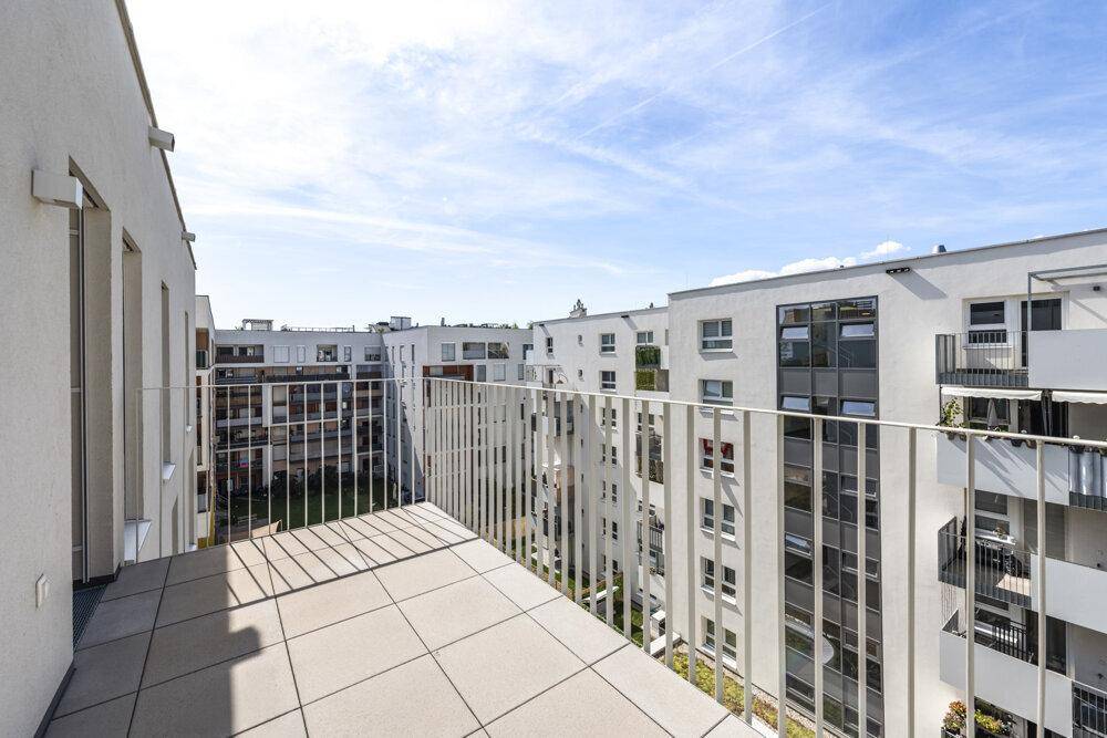 Heller Balkon mit Fliesenboden und weitem Blick über den begrünten Innenhof der Anlage.