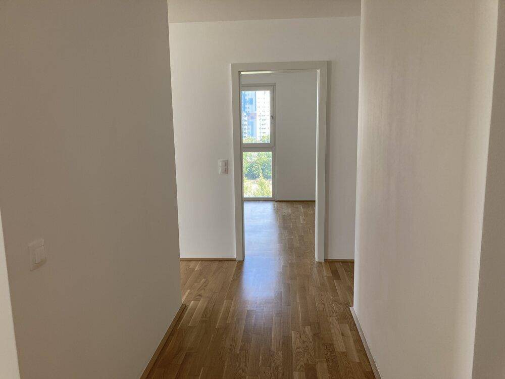Geräumiger Flur mit hellem Parkettboden und Blick in ein Zimmer mit großem Fenster.