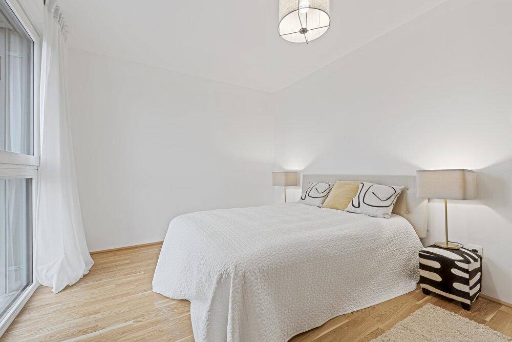 Helles Schlafzimmer mit Doppelbett und Holzboden, direkt neben einem großen Fenster für viel Tageslicht.