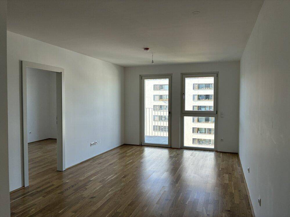 Heller Wohnraum mit Parkettboden und großen Fenstern, die einen Blick auf andere Gebäude bieten.