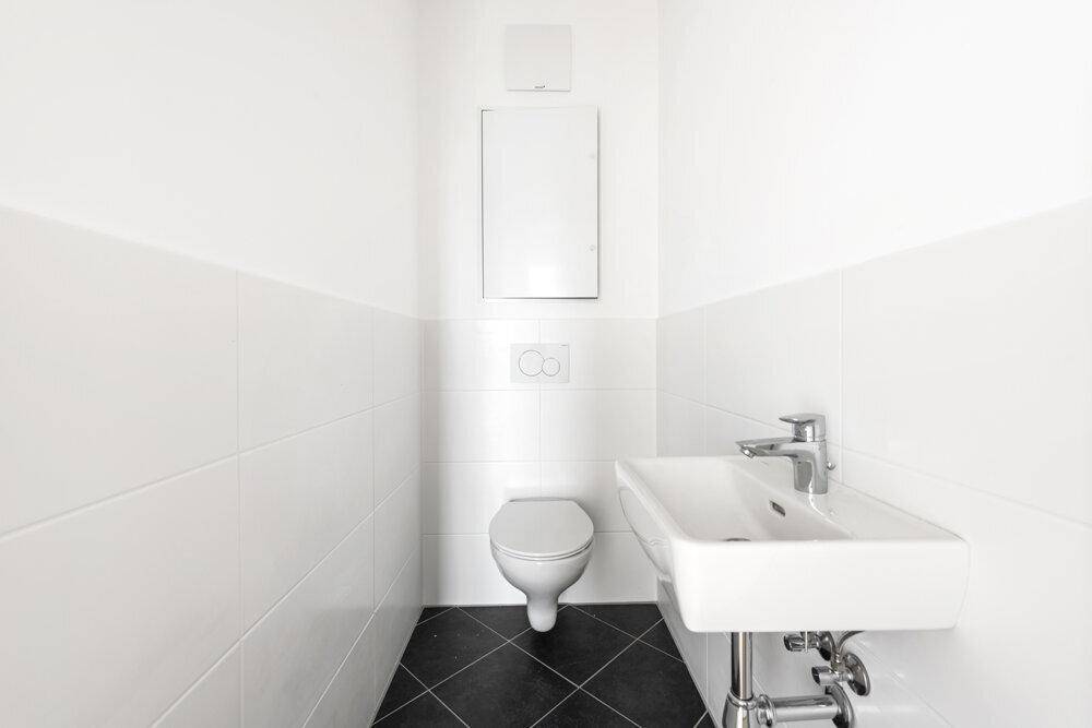 Kleines Gäste-WC mit weißen Fliesen, dunklem Boden und wandhängendem WC.