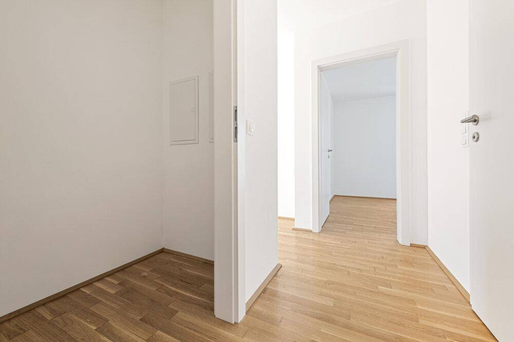 Heller Flur mit Holzboden und weißen Wänden, der zu weiteren Zimmern führt.