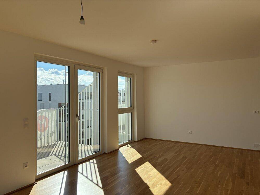 Lichtdurchfluteter Raum mit Parkettboden und Zugang zu einem Balkon.