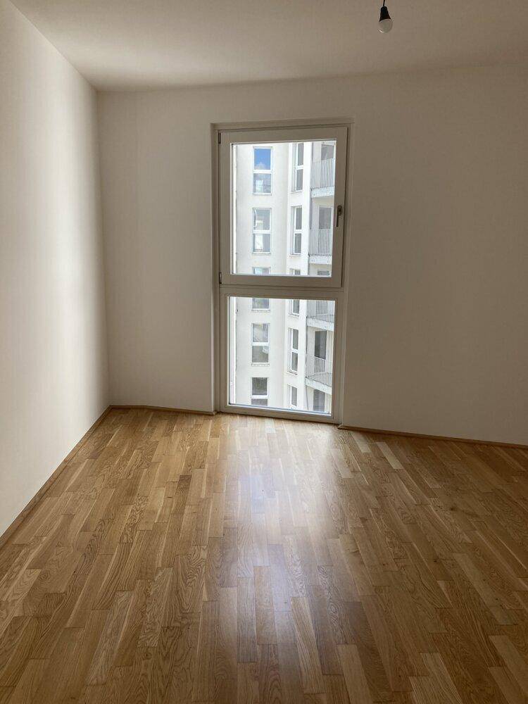 Helles Schlafzimmer mit Parkettboden und einem großen Fenster, das viel Tageslicht hereinlässt.