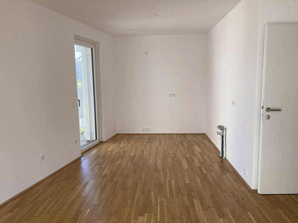 Leerer Raum mit Parkettboden und Zugang zu einem Balkon, ideal für einen Wohnbereich.