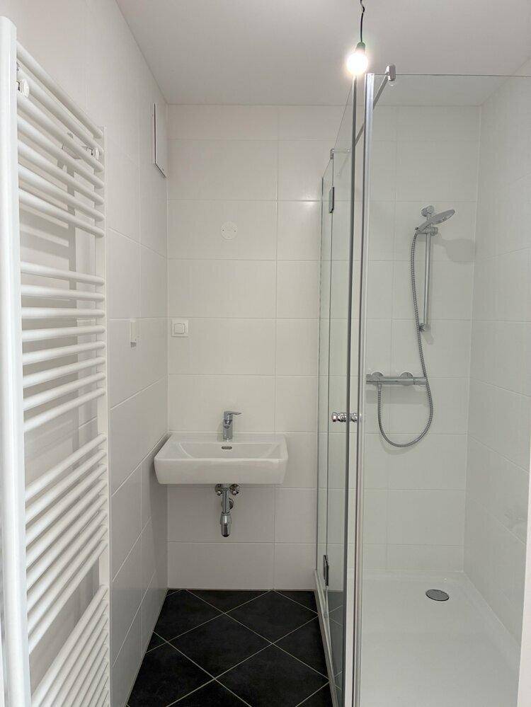 Helles Badezimmer mit Duschkabine, Waschbecken und beheiztem Handtuchhalter, modern gefliest.