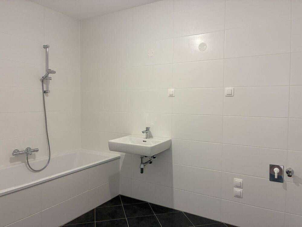 Helles Badezimmer mit Badewanne, Waschbecken und weißen Wandfliesen, bereit zur Nutzung.