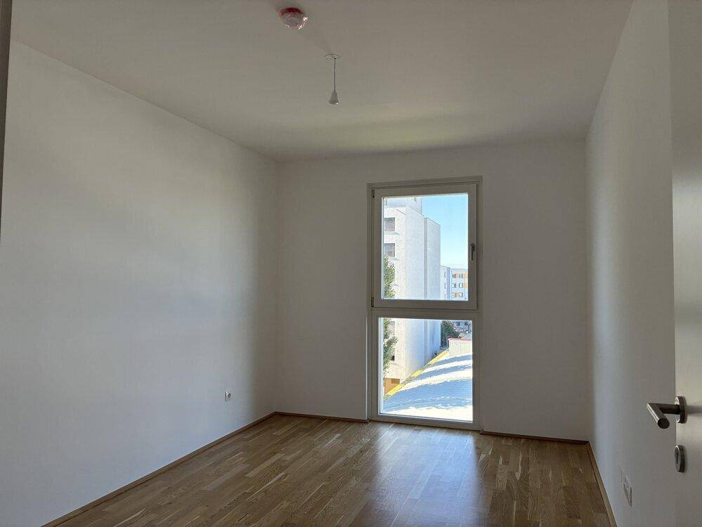 Helles Schlafzimmer mit Parkettboden und großem Fenster, bietet Ausblick.