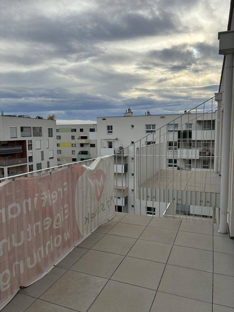 Heller Balkon mit Fliesenboden und Blick auf den Innenhof der Wohnanlage.