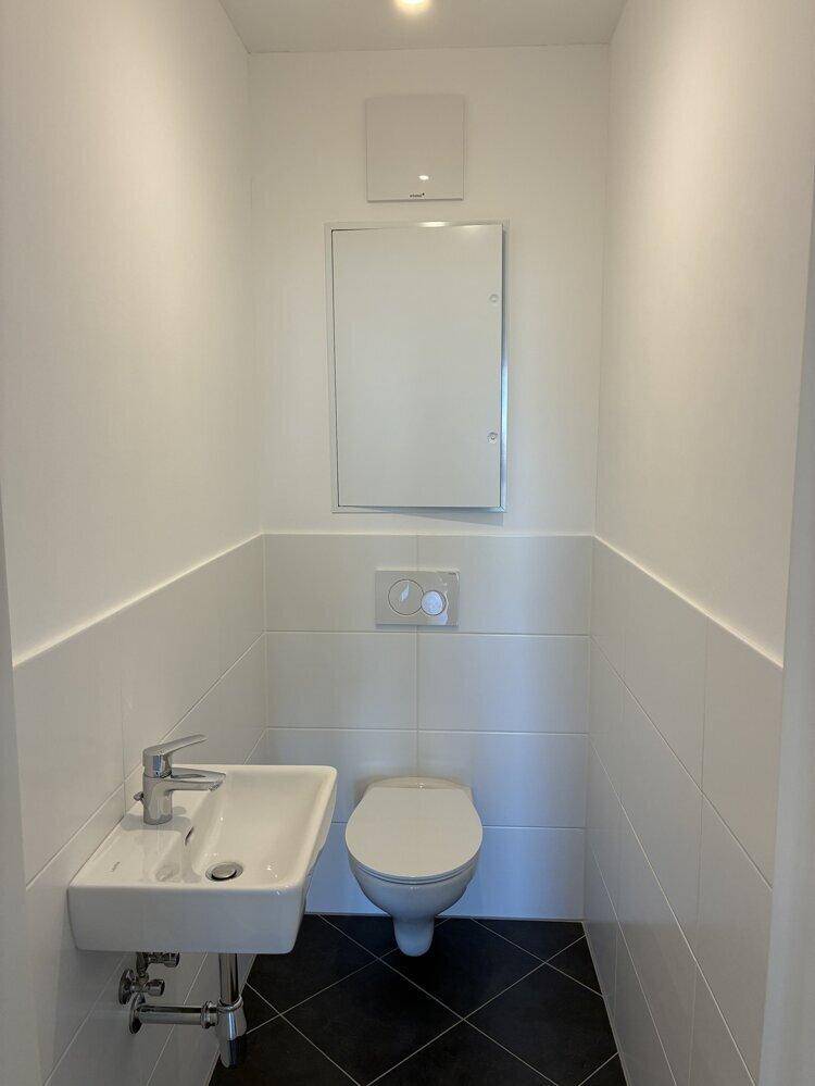 Modernes Gäste-WC mit Wand-WC, kleinem Waschbecken und dunklen Bodenfliesen.