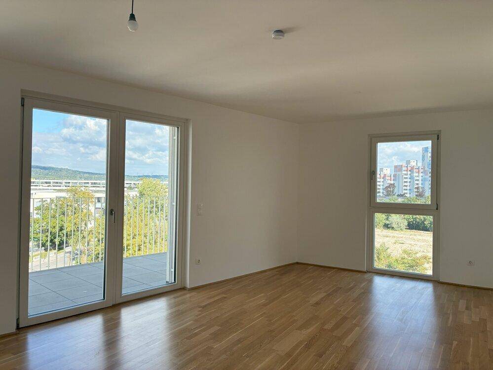 Heller Wohnbereich mit Parkettboden und großen Fenstern, die Zugang zu einer Terrasse bieten und viel Licht spenden.