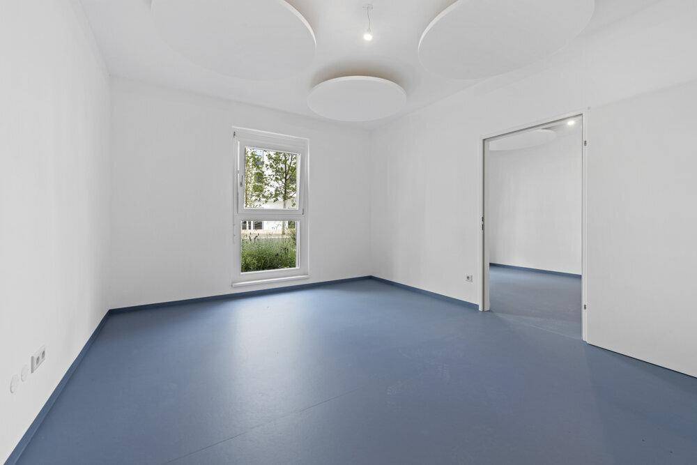 Leerer Raum mit blauer Bodenfläche, weißen Wänden und einem Fenster, das Tageslicht hereinlässt.