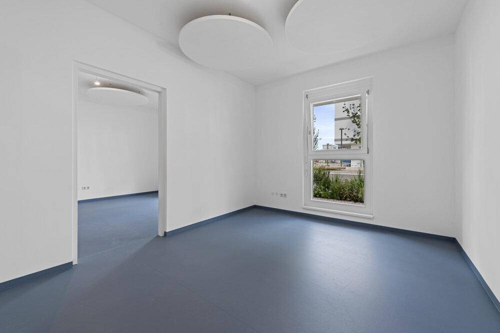 Heller, unmöblierter Raum mit blauer Bodenfläche, weißen Wänden und einem Fenster.
