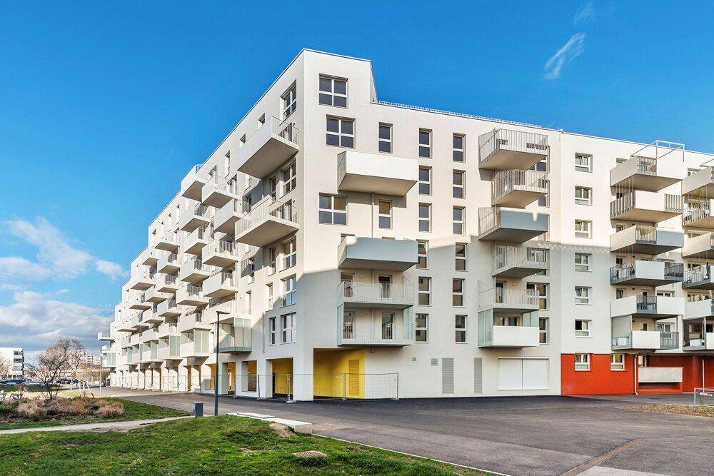 Moderne Wohnanlage mit vielen Balkonen und farbigen Akzenten unter strahlend blauem Himmel.