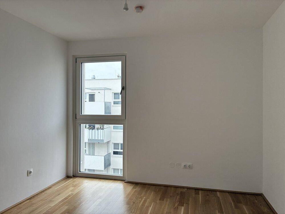 Schlafzimmer mit Parkettboden und großem Fenster, das den Raum mit Licht füllt.