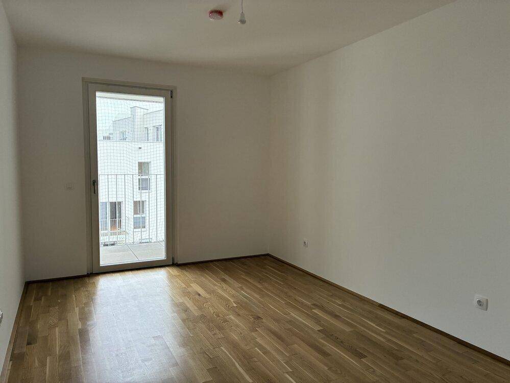 Leeres Schlafzimmer mit Parkettboden und Zugang zu einem französischen Balkon.