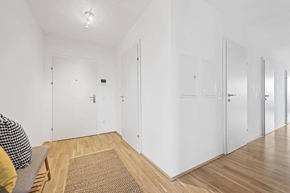 Heller Eingangsbereich mit Holzboden und weißen Türen, der zu den verschiedenen Räumen führt.