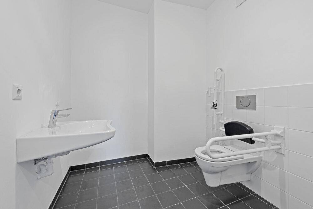 Barrierefreies Badezimmer mit wandhängendem WC, Haltegriffen und modernem Waschbecken.
