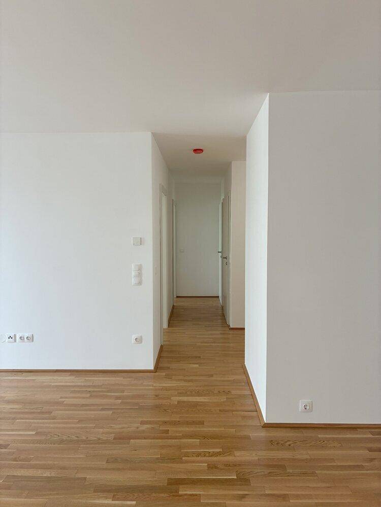 Langer, heller Flur mit Holzboden und weißen Wänden, der zu weiteren Räumen der Wohnung führt.