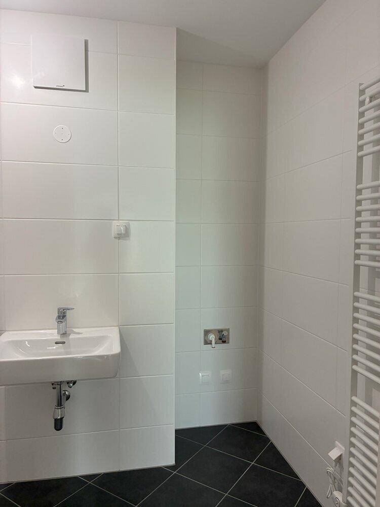 Modernes WC mit weißen Wandfliesen, schwarzem Boden und einem Waschbecken, sauber und funktional.