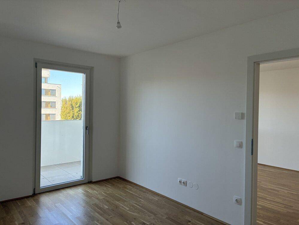 Helles Schlafzimmer mit Parkettboden und direktem Zugang zu einem Balkon mit Blick auf die Nachbarschaft.