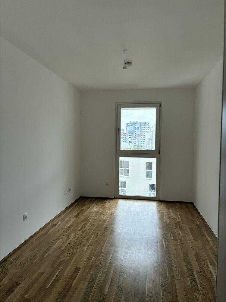 Helles, unmöbliertes Zimmer mit Parkettboden und großem Fenster mit Blick auf die Stadt.