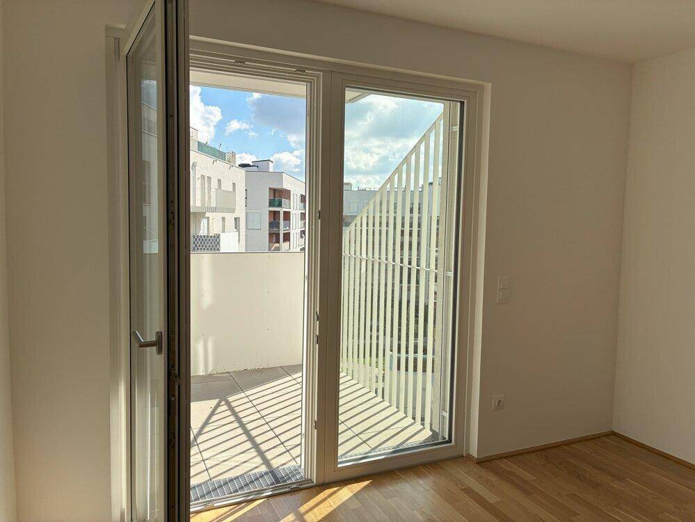 Heller Raum mit geöffneter Balkontür, die einen Blick auf die umliegenden Gebäude freigibt.