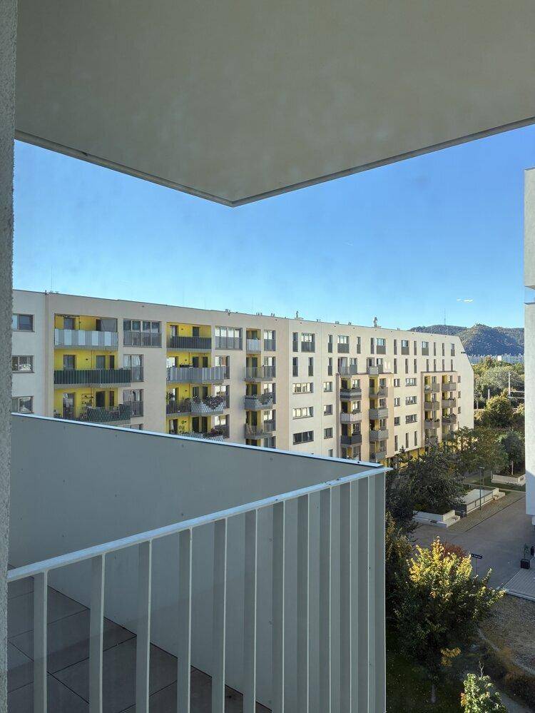 Ausblick von einem Balkon auf umliegende Wohngebäude und eine hügelige Landschaft.
