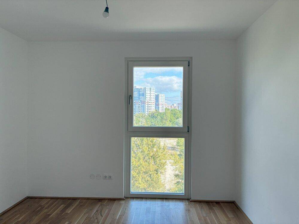 Heller Raum mit Holzboden und großem Fenster, das einen weiten Blick auf die Stadt bietet.