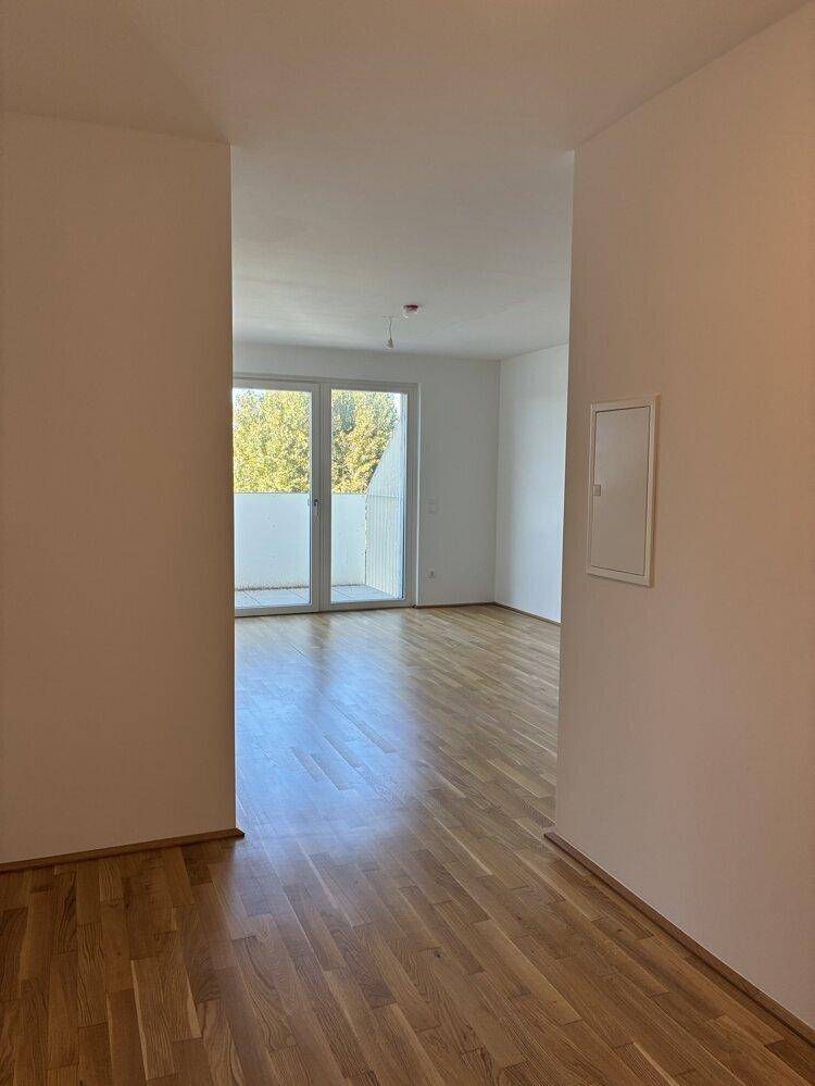 Heller Wohnraum mit Parkettboden und Zugang zu einem Balkon mit Blick ins Grüne.