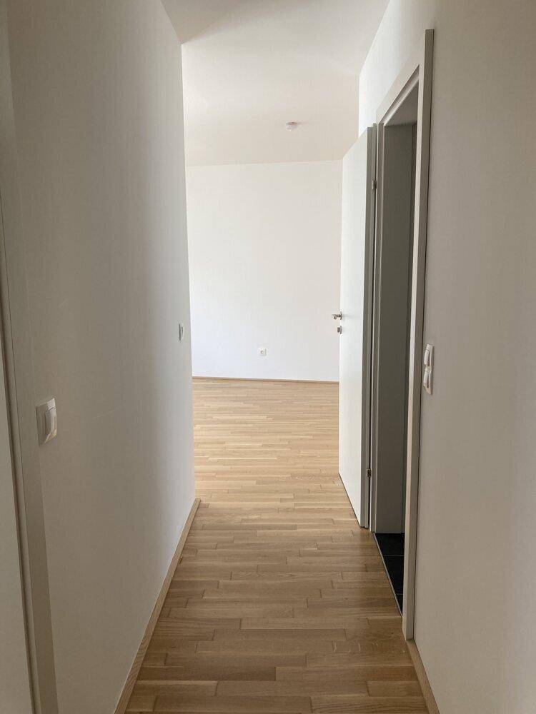 Schmaler Flur mit Parkettboden und einer offenen Tür, die den Blick in einen weiteren Raum freigibt.
