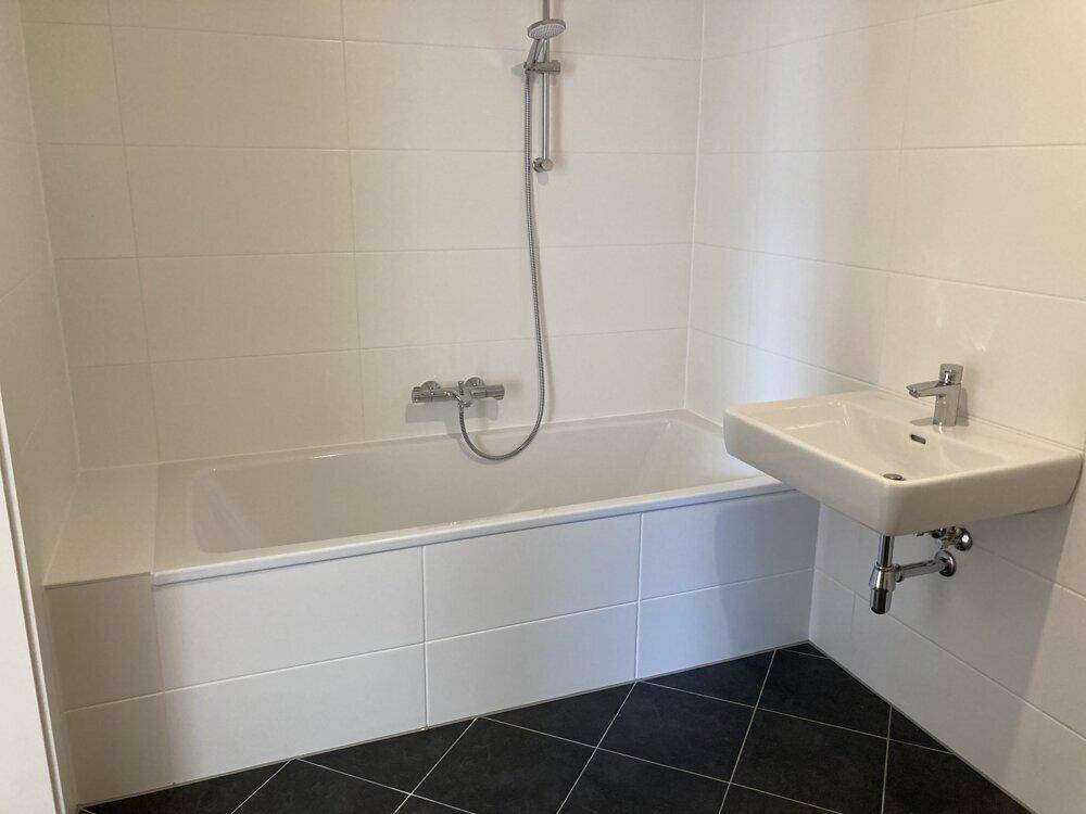 Badezimmer mit Badewanne, Waschbecken und weißen Wandfliesen auf dunklem Fliesenboden.