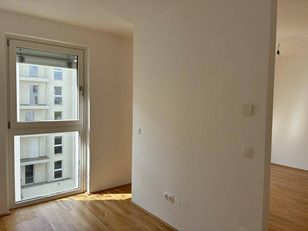 Heller Raum mit Parkettboden und großem Fenster, Blick auf das gegenüberliegende Gebäude.