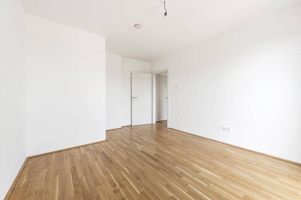 Geräumiges Zimmer mit Holzboden und weiß gestrichenen Wänden, ideal als Schlafzimmer.