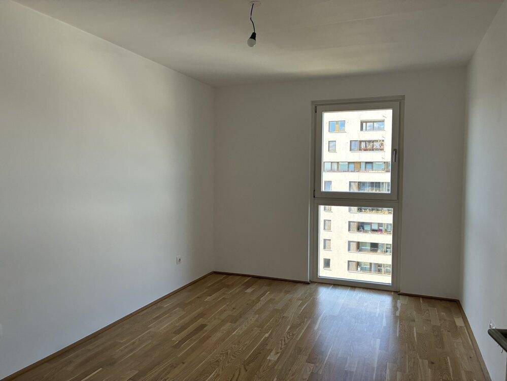 Leeres Schlafzimmer mit Holzboden und einem großen Fenster mit Blick ins Grüne.