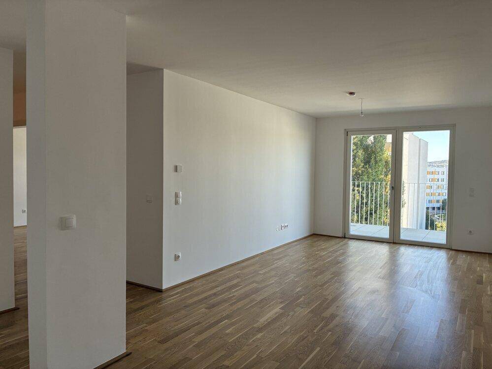 Geräumiges Wohnzimmer mit Parkettboden und Zugang zu einem Balkon, hell und modern.