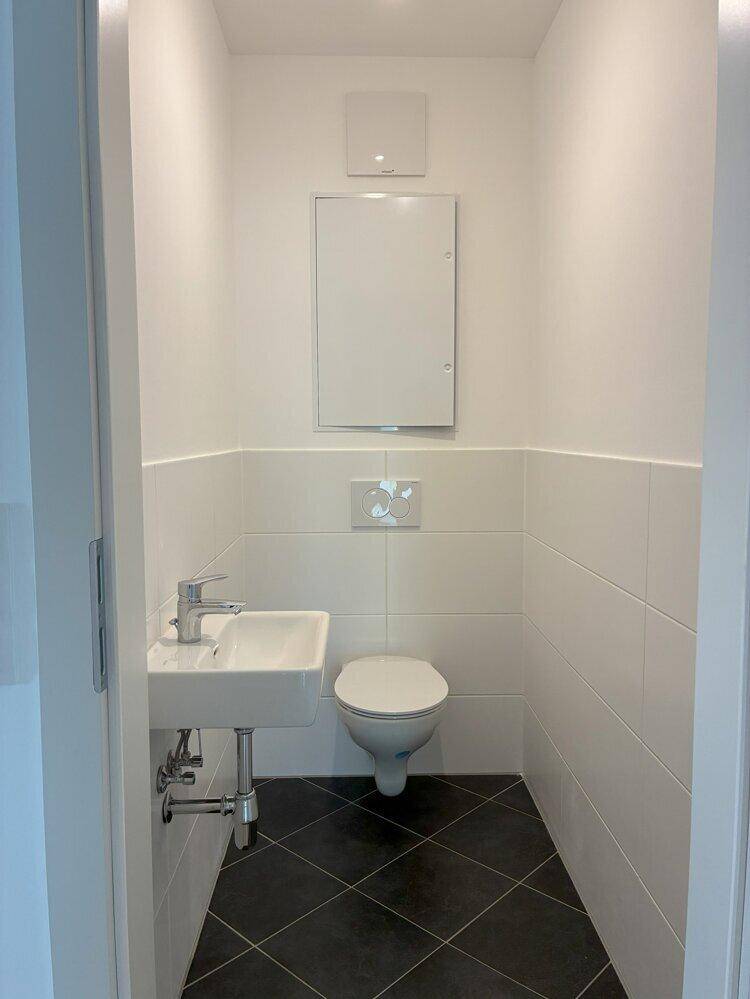 Separates Gäste-WC mit Wand-WC, kleinem Waschbecken und dunklem Fliesenboden.