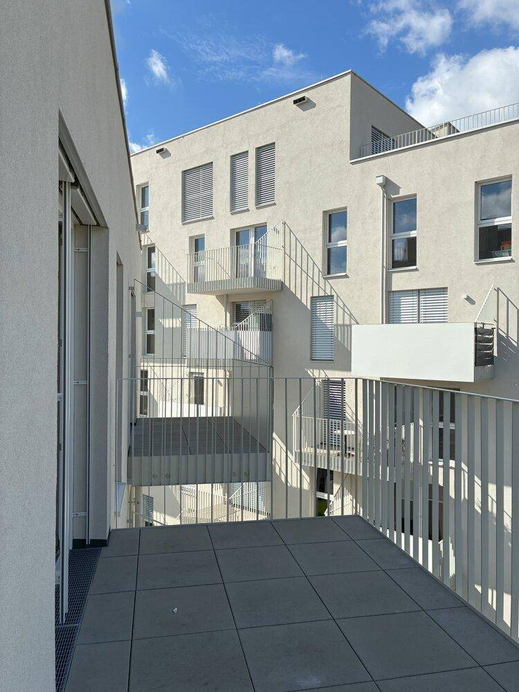 Geräumiger Balkon mit Fliesenboden und Blick auf den Innenhof der modernen Wohnanlage.