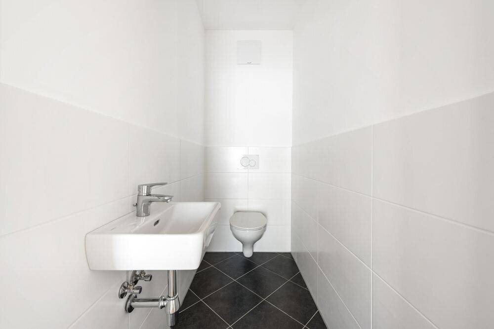 Separates Gäste-WC mit wandhängender Toilette, kleinem Waschbecken und dunklen Bodenfliesen.