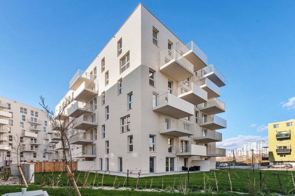 Eckansicht eines modernen Wohngebäudes mit zahlreichen Balkonen und gepflegter Grünfläche im Vordergrund.