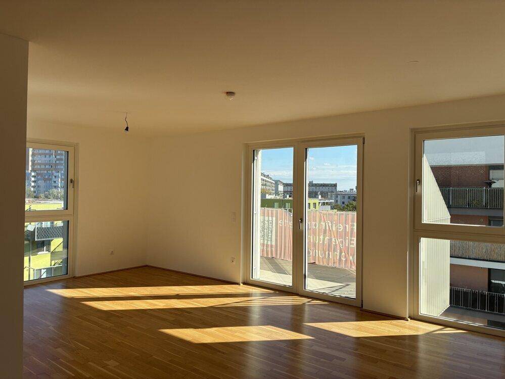 Heller Wohnbereich mit Parkettboden und Zugang zu einem Balkon, viel Tageslicht.