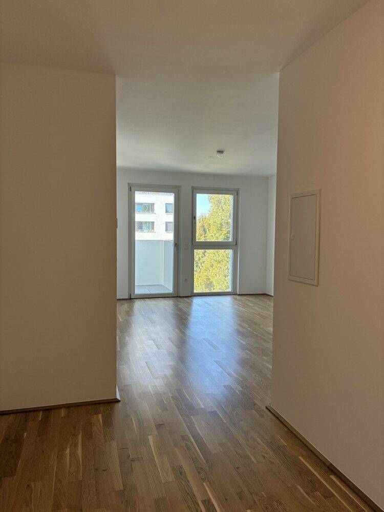 Lichtdurchfluteter Raum mit Parkettboden und Zugang zu einem Balkon mit grüner Aussicht.