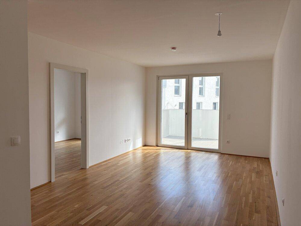 Geräumiges Wohnzimmer mit hellem Parkettboden und großen Fenstern, die viel Tageslicht hereinlassen.