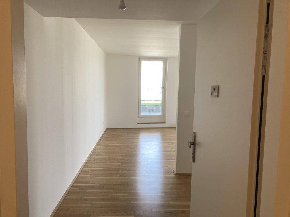 Heller Flur mit Eichenparkettboden und weißen Wänden, der zu einem weiteren Raum führt.