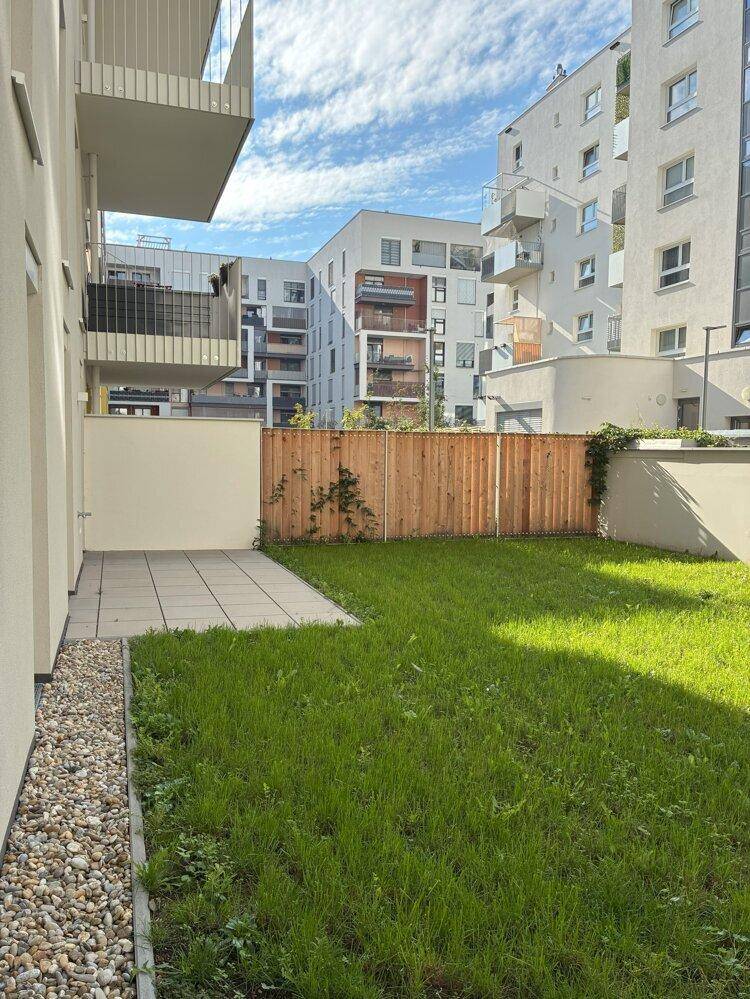Privater Gartenbereich mit Terrasse und Rasenfläche, umgeben von modernen Wohngebäuden.
