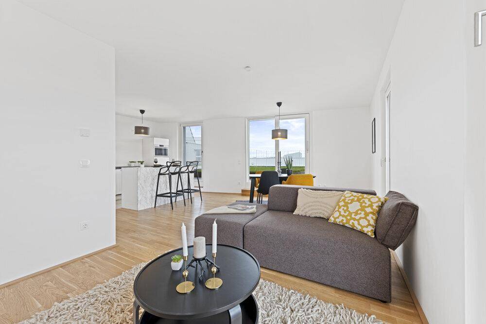 Lichtdurchfluteter Wohnbereich mit gemütlichem Sofa, Couchtisch und offenem Übergang zur Küche.